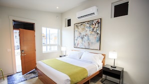 A bedroom with a wooden bed, a nightstand, a wall-mounted air conditioner, and a large abstract painting. - The Drift (Pagosa Springs)