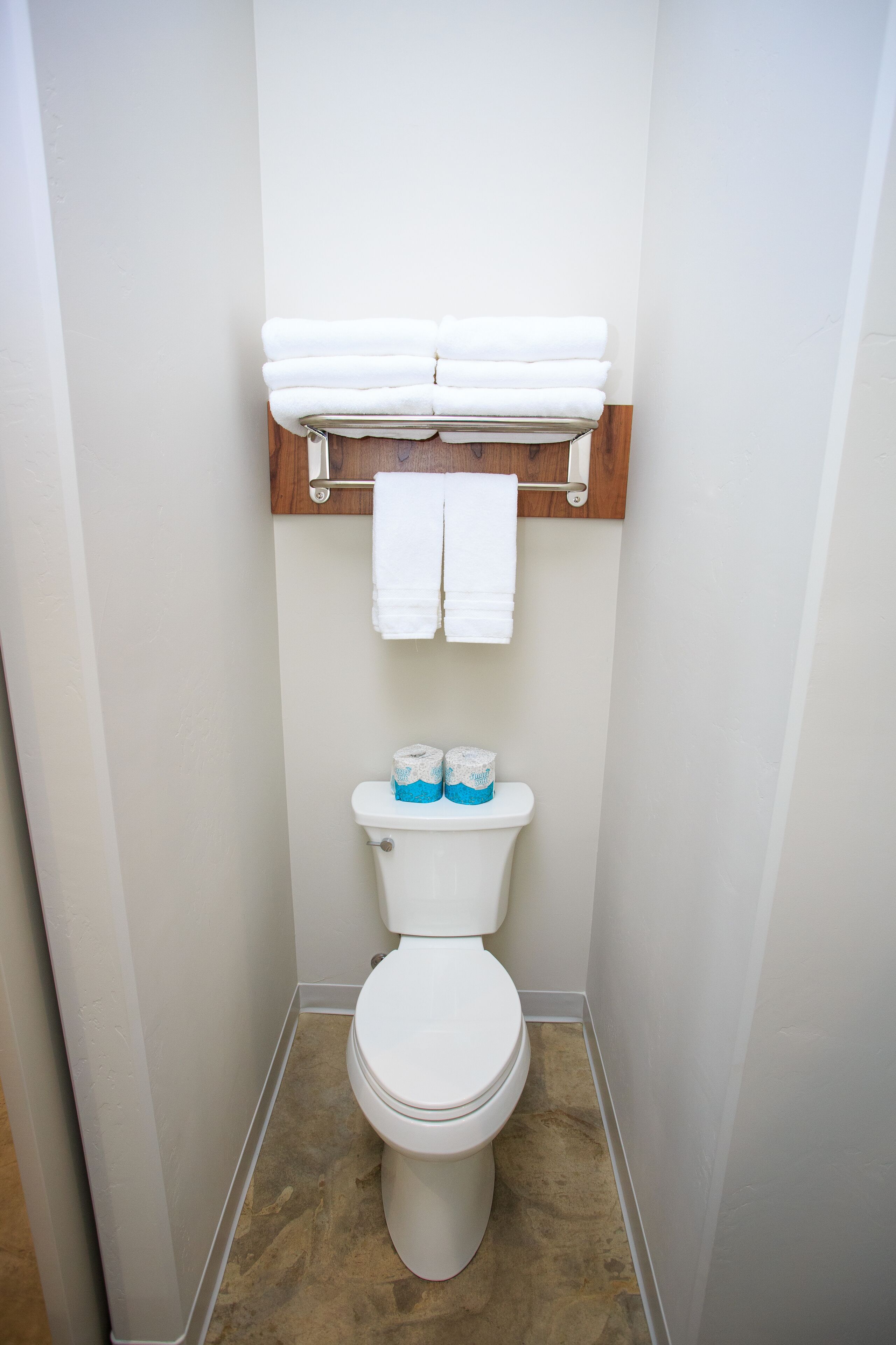 A small, clean bathroom with a toilet, a towel rack, and a roll of toilet paper.