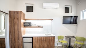 A compact kitchen with a refrigerator, microwave, and sink. There are two green chairs and a small table. - The Drift (Pagosa Springs)