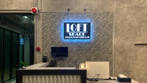A reception desk with a 'LOFT SPACE' sign, a flat-screen TV, and a computer on the counter. - Loft Space Hotel (Ranong)