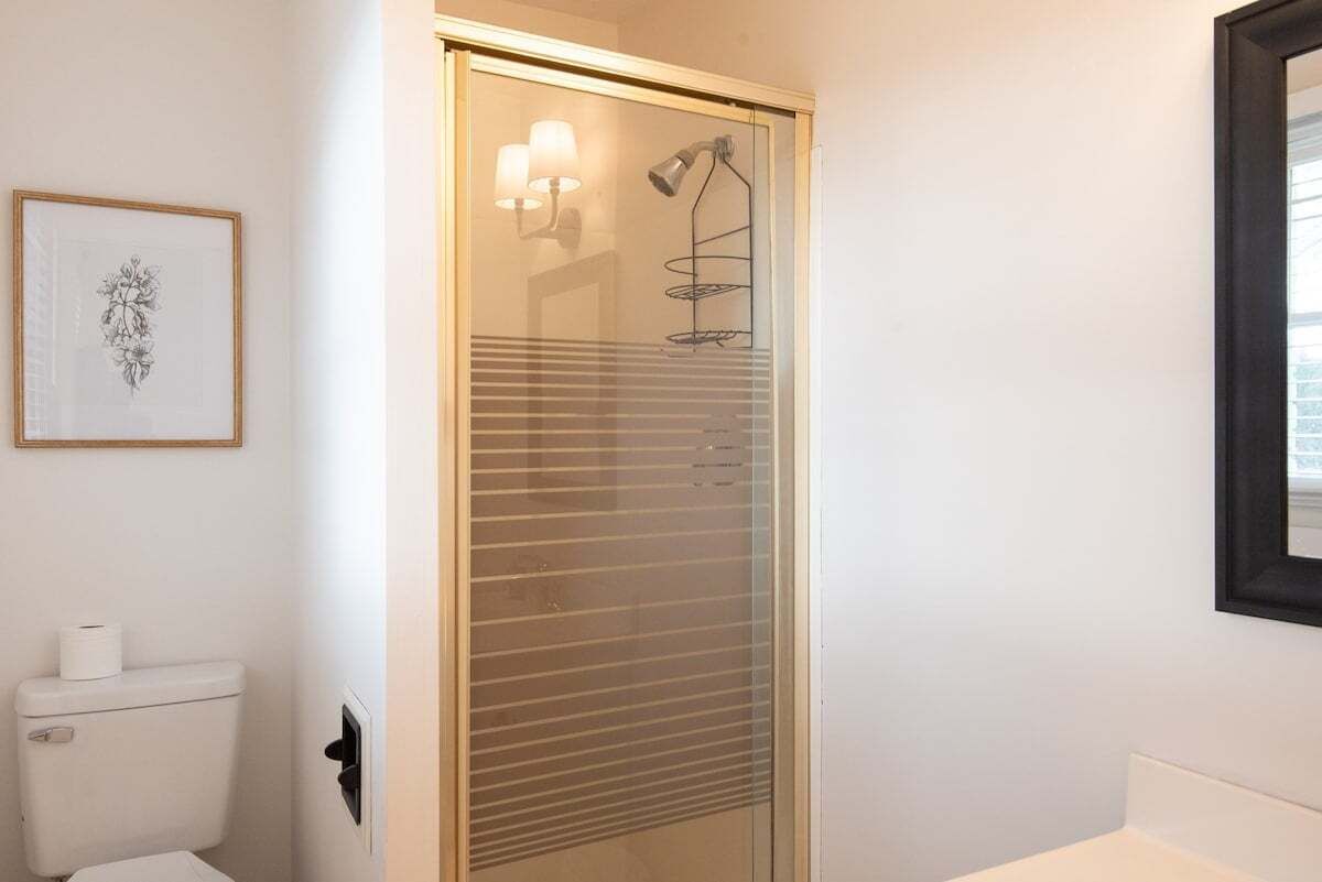A bathroom with a toilet, a framed artwork, a shower with a glass door, and a wall-mounted light fixture.