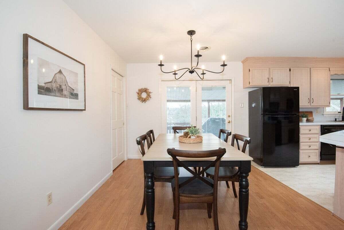 Een eetruimte met een tafel, stoelen, een kroonluchter, een koelkast en houten kasten.