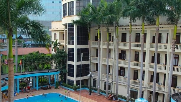 A hotel with a swimming pool, multiple balconies, and a covered area with umbrellas.