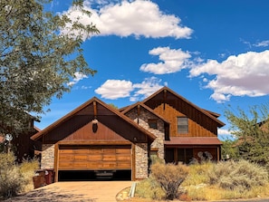 A two-story house with a stone foundation and wooden siding, featuring a garage and a second-story balcony.