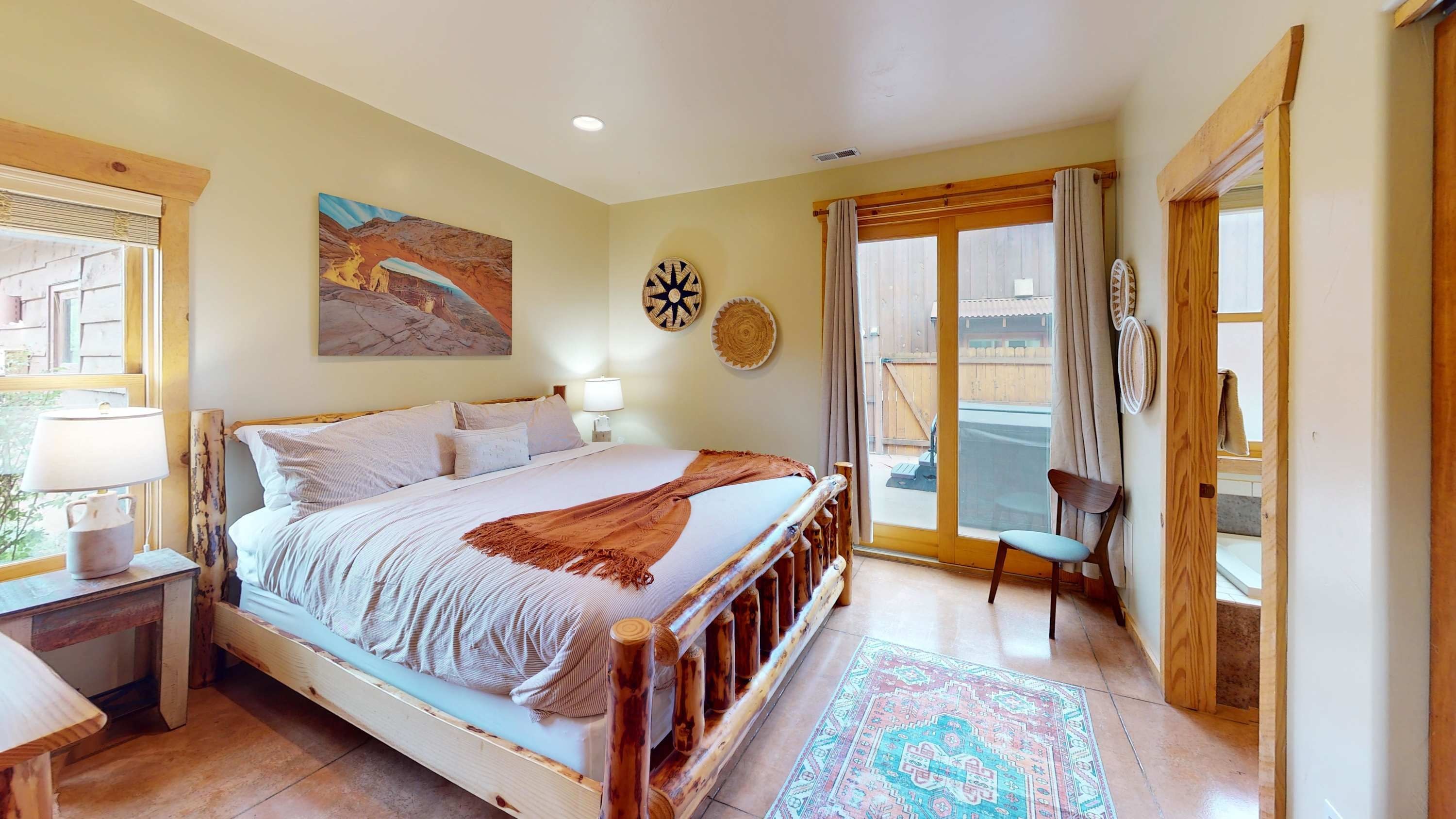 A bedroom with a bed, bedside table, lamp, and a view of the outside.