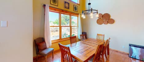 Un espace repas comprenant une table et des chaises en bois, un banc, une fenêtre avec des rideaux et des œuvres d’art murales.