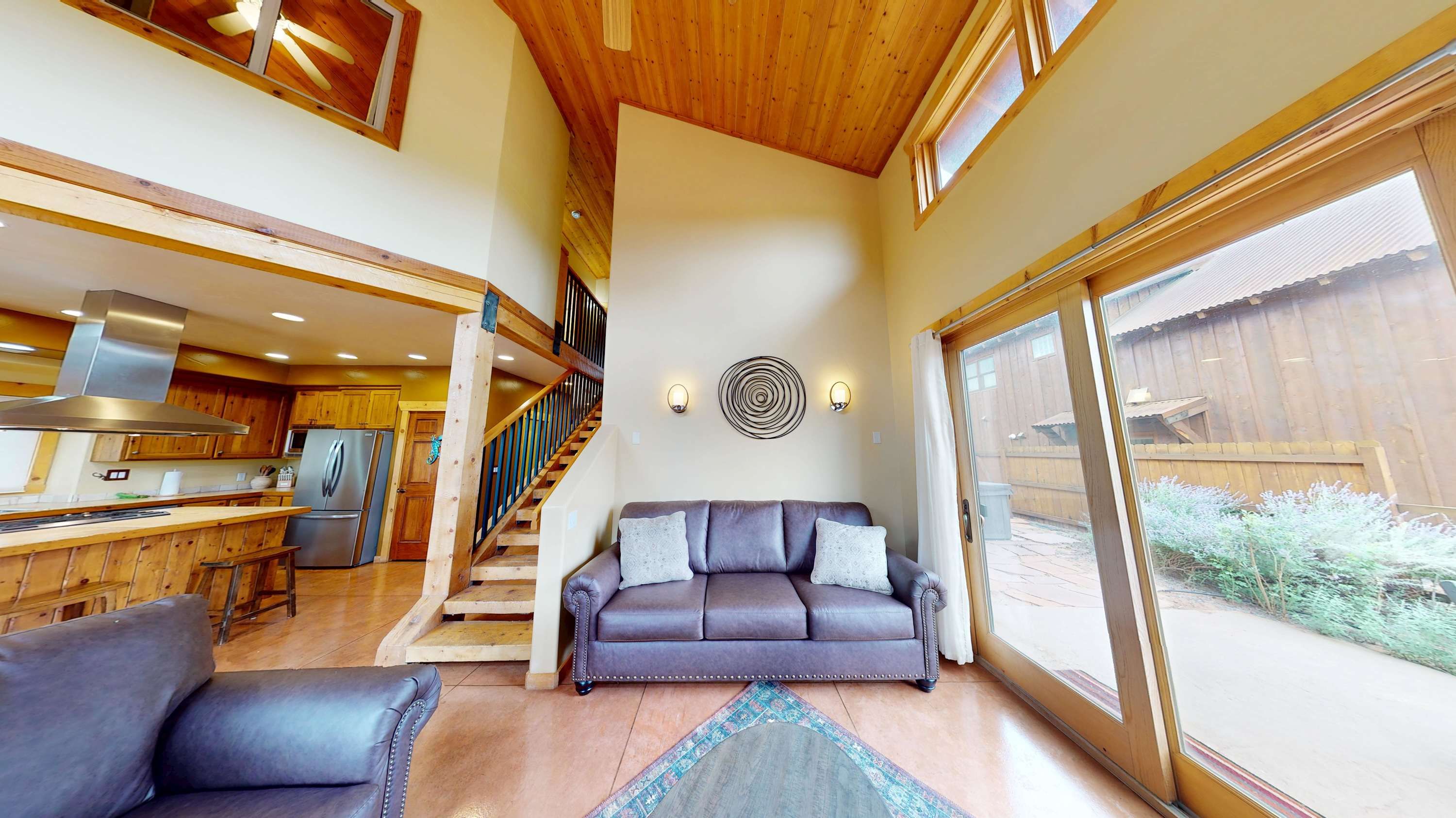 A spacious living area with a sofa, a dining area with wooden cabinets, and a kitchen with stainless steel appliances.