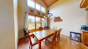 A dining area with a wooden table and chairs, a coffee machine, and a view of the outdoors through large windows. - Coyote Run - 4 (Moab)