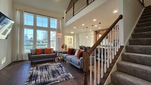 A spacious living area with a staircase, large windows, and a dining area.
