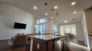 Una cocina moderna con una isla central, iluminación colgante y un amplio ventanal que proporciona luz natural.