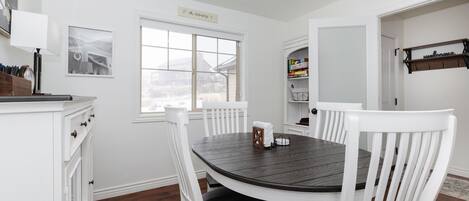 A dining room with a round table, white chairs, and a window.