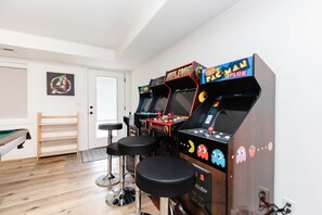 Una habitación con tres máquinas de arcade, una mesa de billar y un banco de madera.