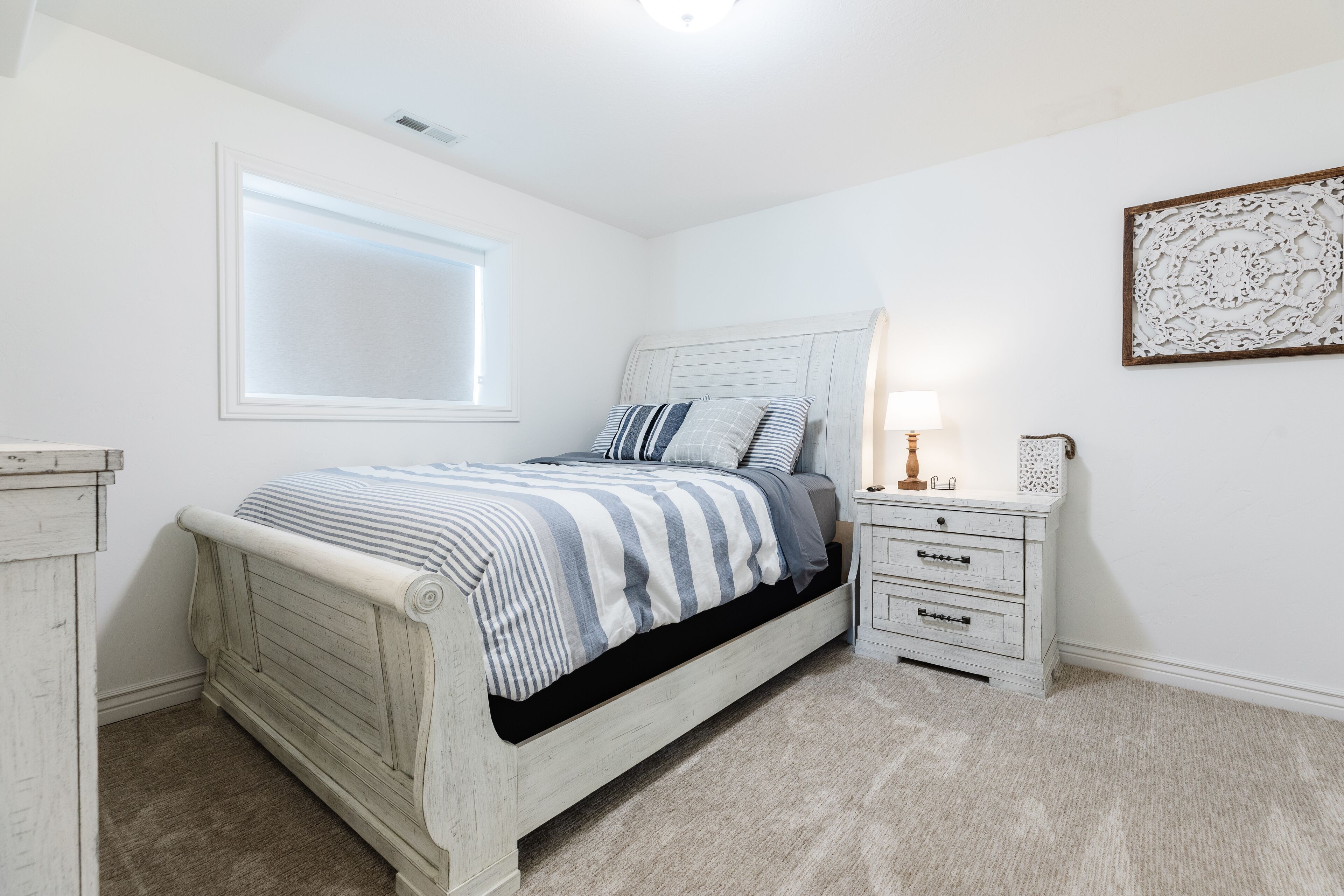 A bedroom with a bed, a nightstand, a lamp, and a wall decoration.