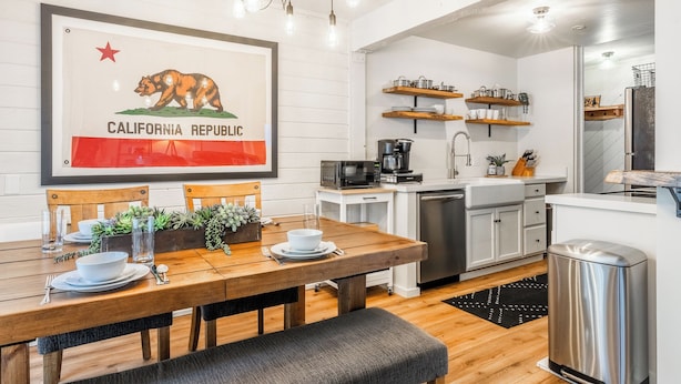 A modern kitchen with a dining area, featuring a wooden table, chairs, a coffee machine, and a sink.