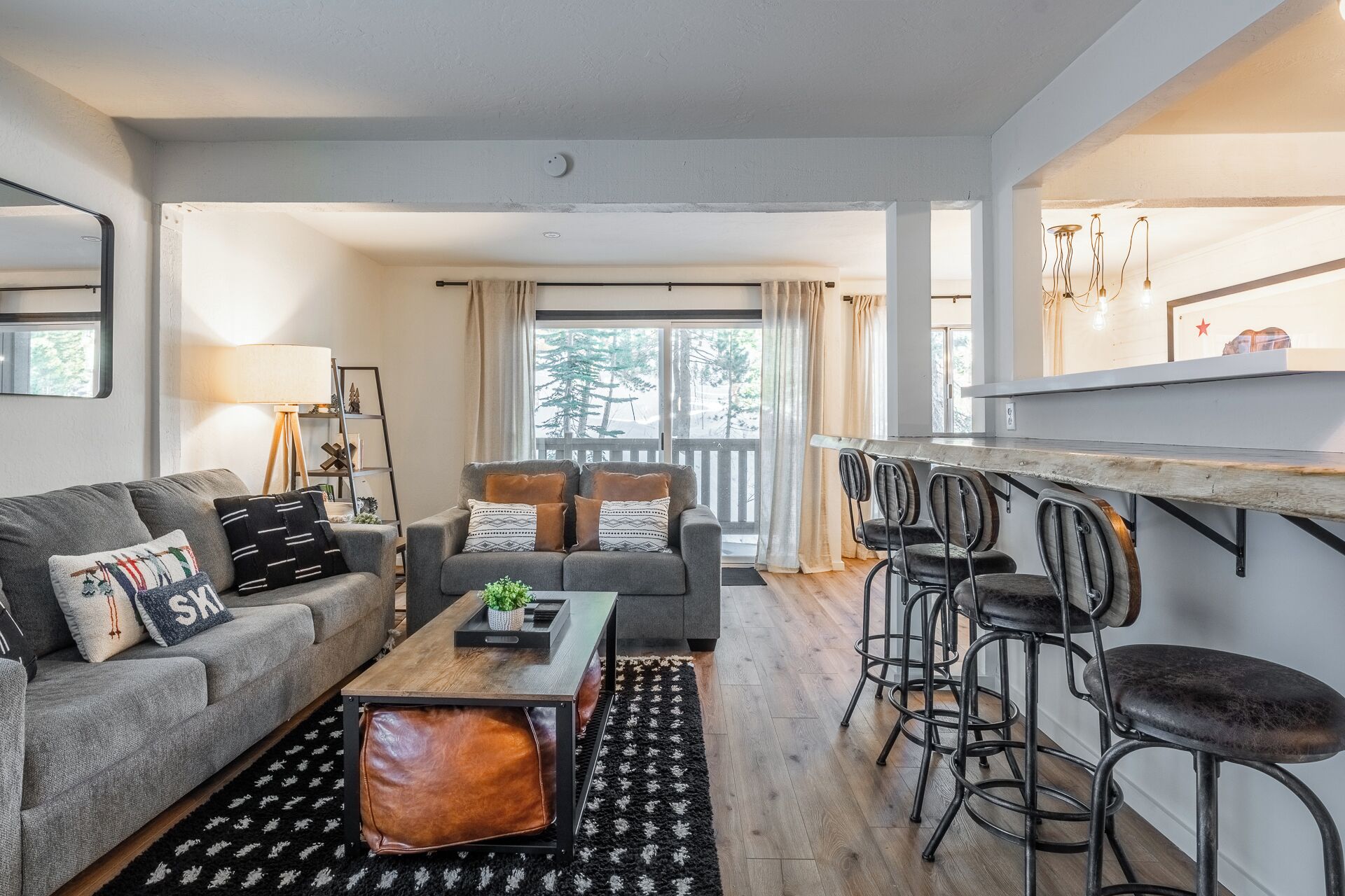A modern living room with a grey sofa, a coffee table, and a bar area with stools.