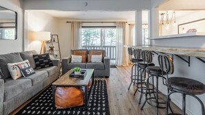 A modern living room with a grey sofa, a coffee table, and a bar area with stools.