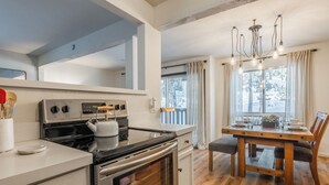 A modern kitchen with stainless steel appliances, a wooden dining table, and a chandelier.