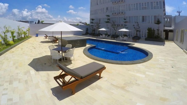 Un área de piscina en la azotea con sillones y sombrillas, rodeada por un edificio moderno.