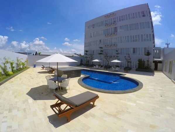Un espace piscine aménagé sur le toit, avec des chaises longues et des parasols, entouré d’un bâtiment moderne.