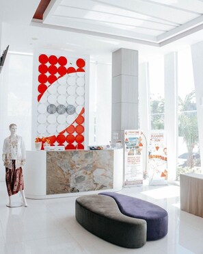 Un espace d’accueil moderne avec un comptoir en marbre, une grande horloge murale et un coin salon.