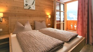 Une pièce aux murs lambrés, comprenant un lit, deux oreillers, une table de chevet, une lampe fixée au mur et une fenêtre donnant sur un paysage montagneux.