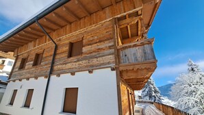 Un chalet en bois à la façade blanche, doté de balcons en bois et d’une base en pierre.