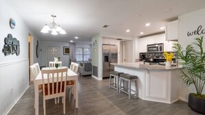 Una cocina moderna con armarios blancos, una isla central y un comedor con mesa y sillas de madera.