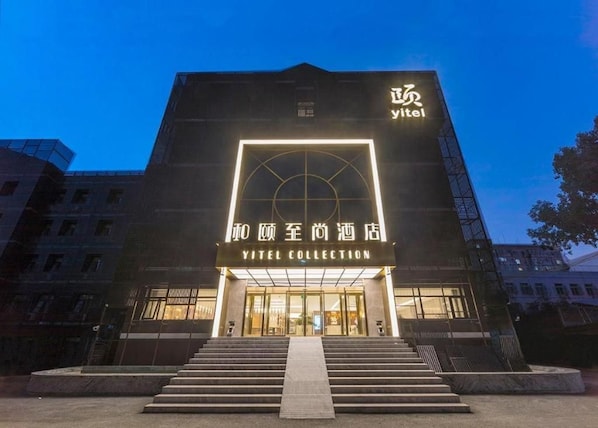 A hotel entrance with a modern design, featuring a prominent sign for 'Yitel Collection' and a staircase leading to the entrance.