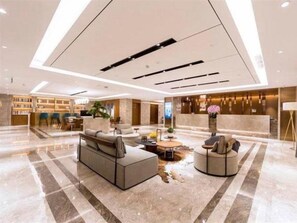 A modern hotel lobby with a reception desk, seating area, and a bar.