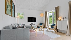 A modern living room with a grey sofa, a wooden coffee table, a TV, and a large window with curtains.