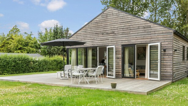 A wooden cabin with a deck, outdoor seating, and sliding glass doors.