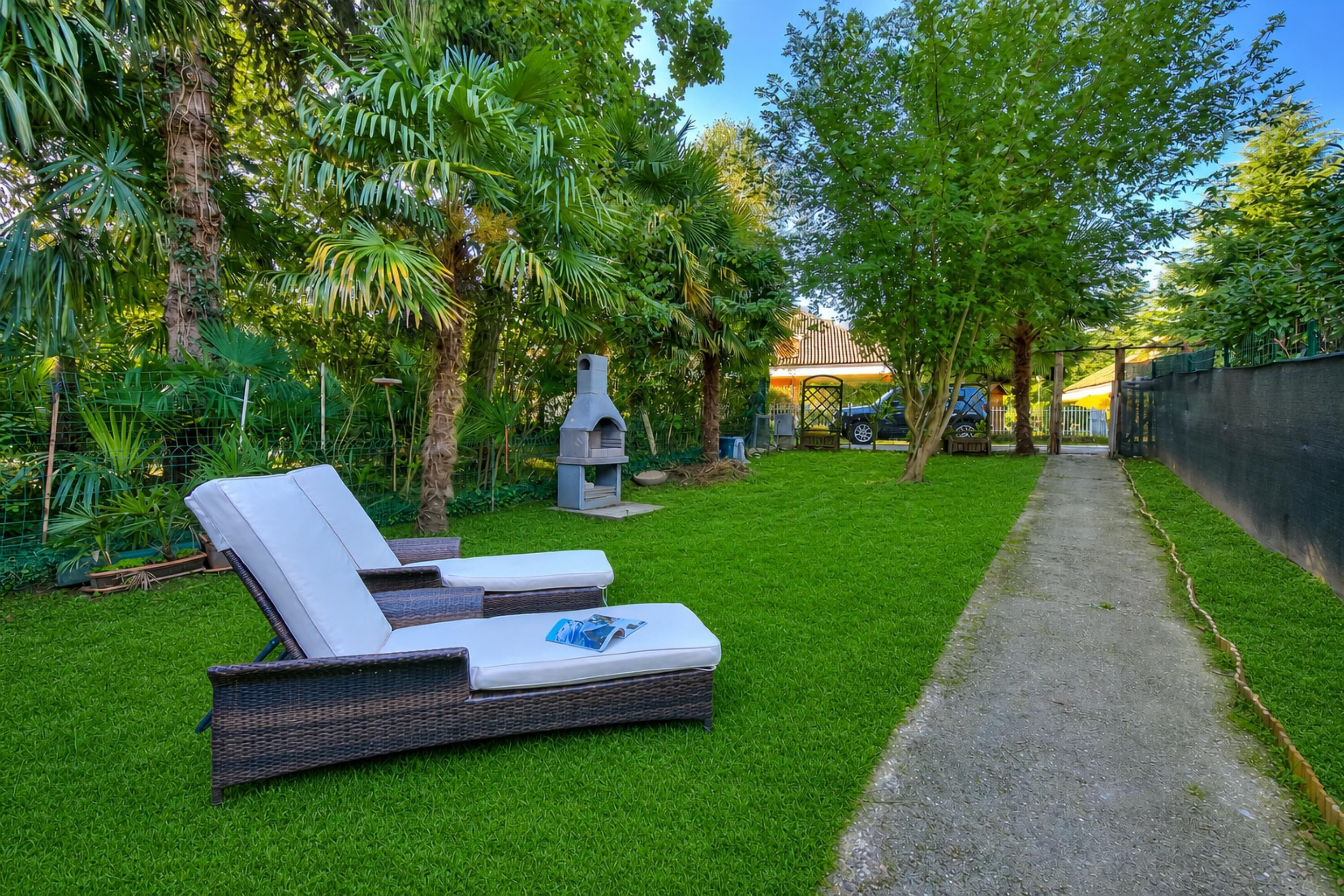 A backyard with two lounge chairs, a grill, and a paved path.
