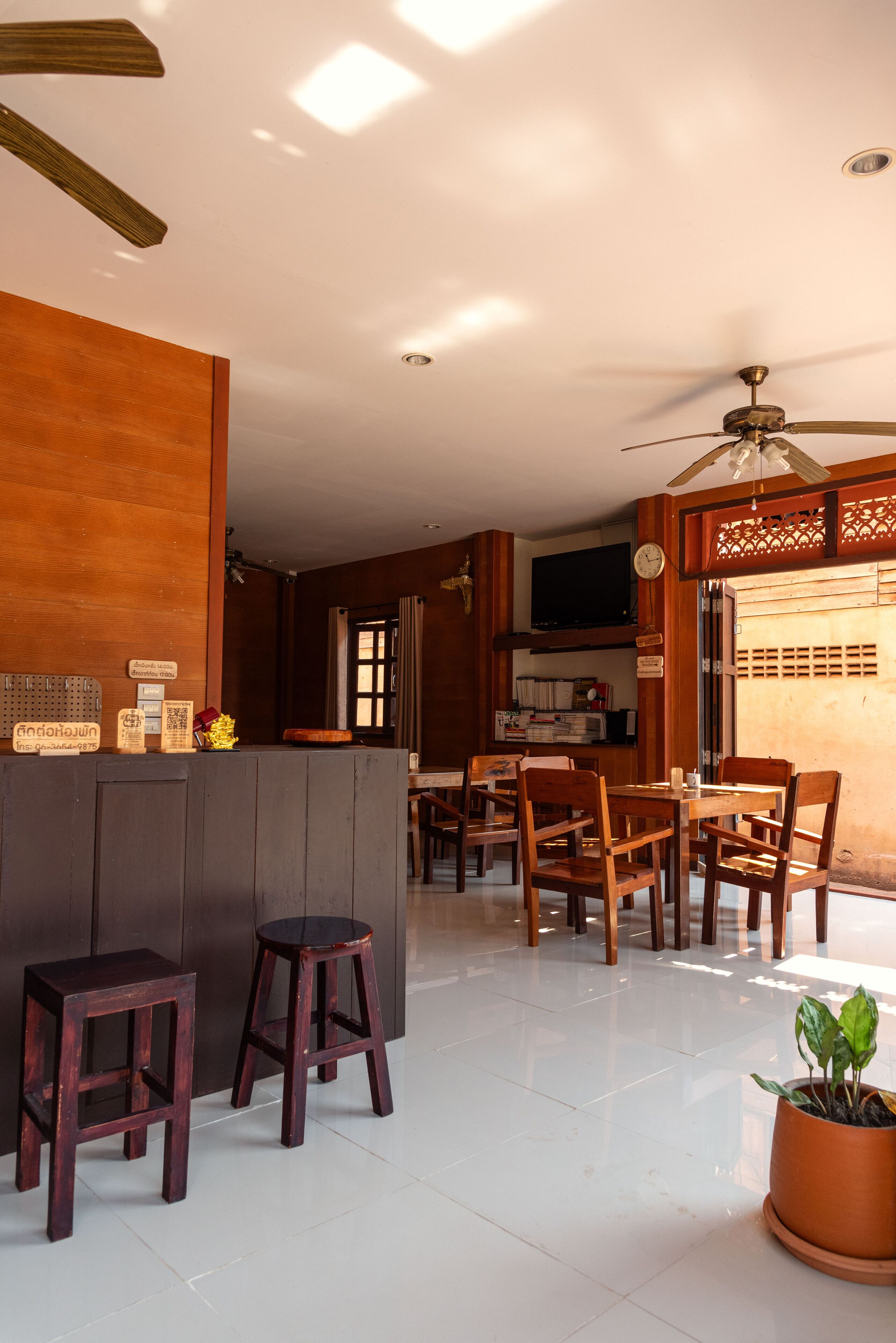 A modern interior with a wooden reception desk, bar stools, a dining area with chairs, a ceiling fan, and a television.