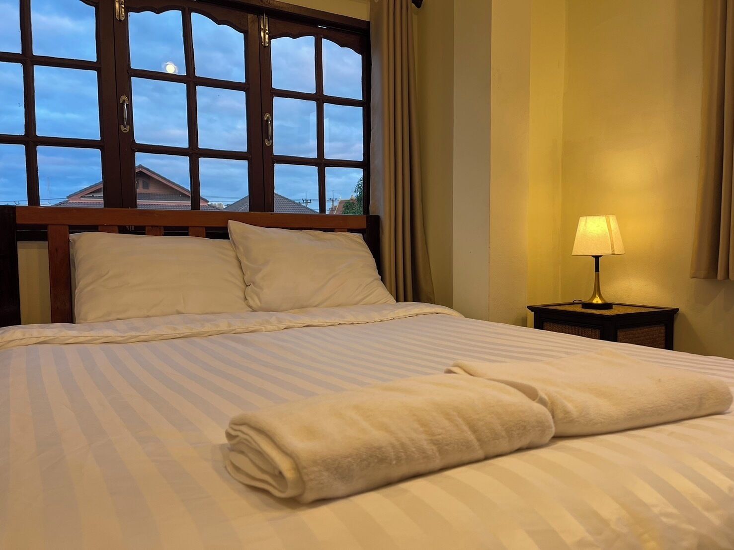 A neatly made bed with a striped bedspread, a rolled towel, and a bedside lamp.
