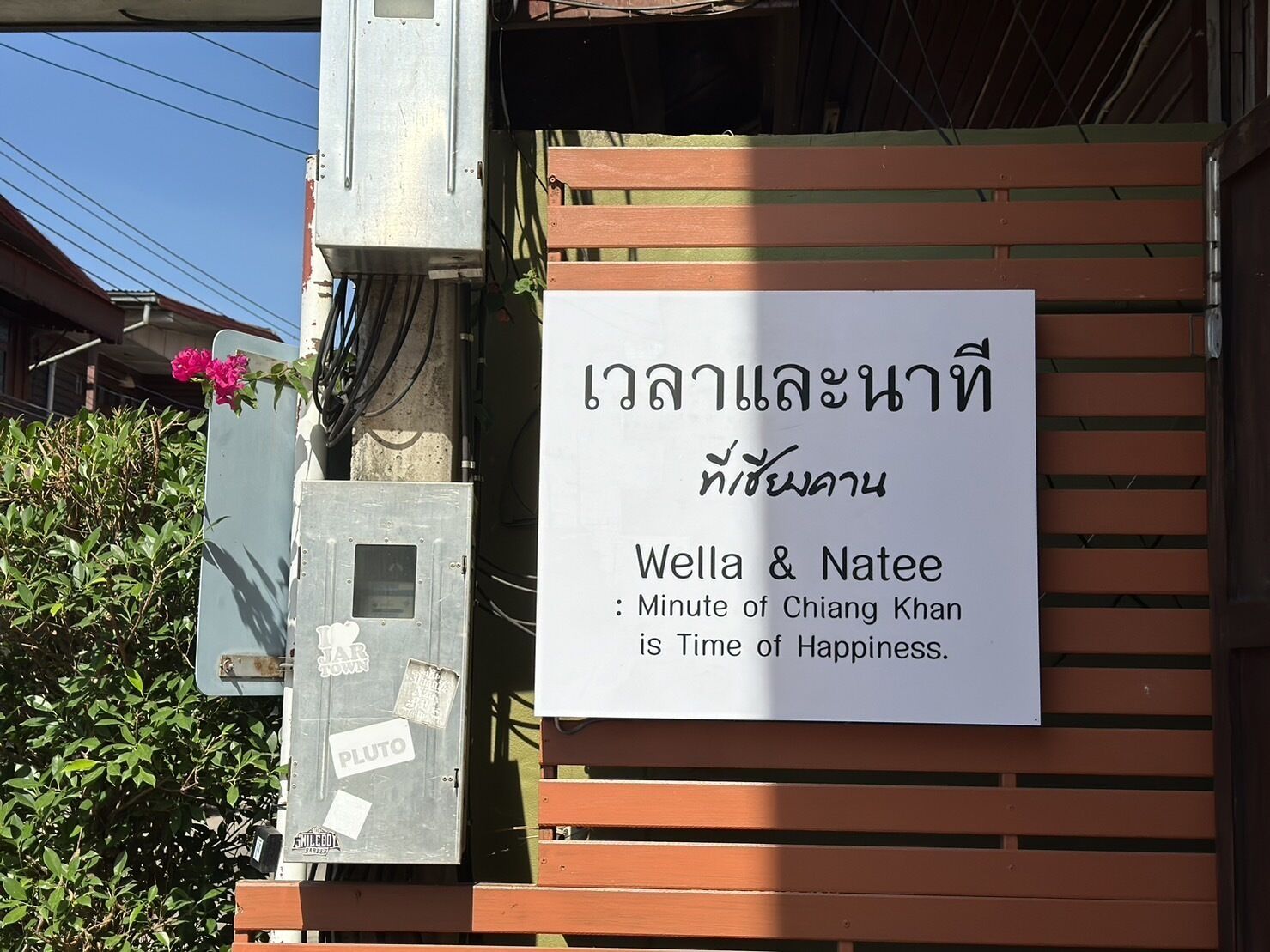 A sign with Thai text and a message in English, placed on a wooden structure.