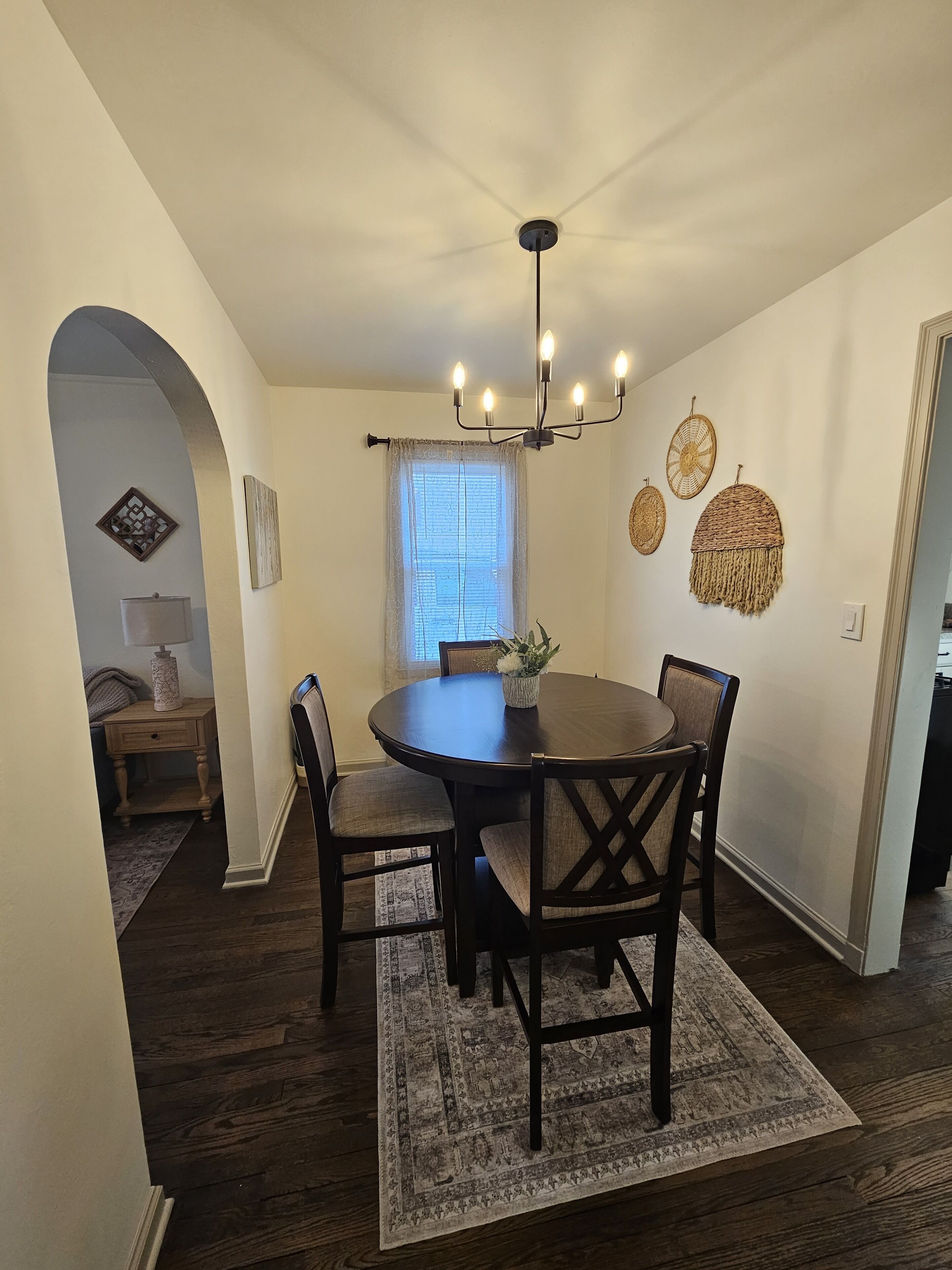 A dining area with a round table, chairs, a chandelier, and a patterned rug.