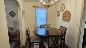 A dining area with a round table, chairs, a chandelier, and a patterned rug.