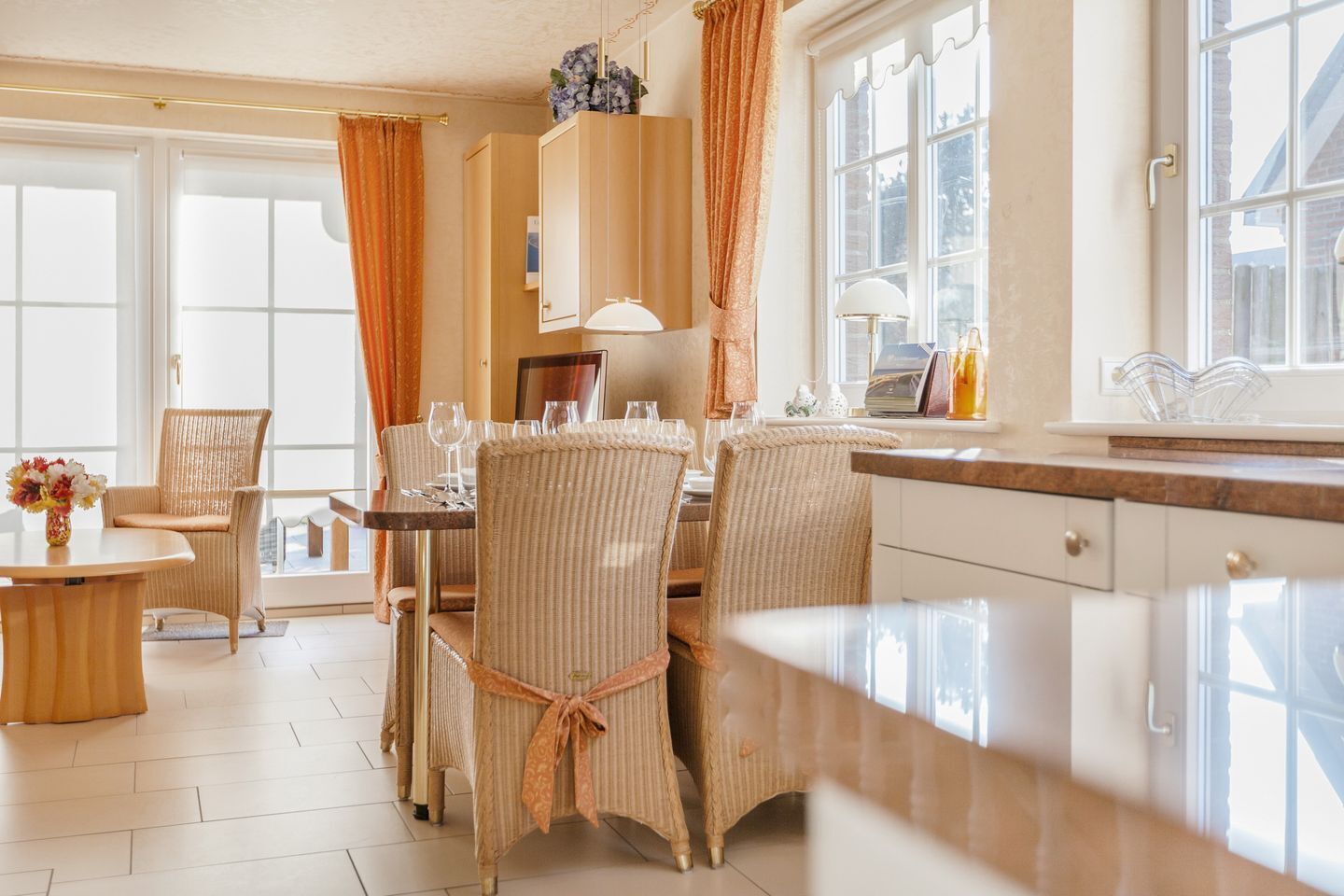 Een eethoek met rieten stoelen, een ronde tafel en een laptop op het aanrecht.