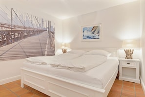 A bedroom with a large bed, two bedside tables, a nightstand, a wall-mounted lamp, and a cityscape painting.