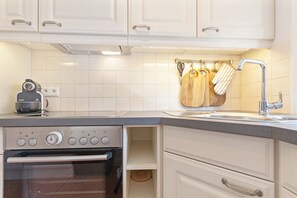A modern kitchen with white cabinets, a built-in oven, a stainless steel range, and a hanging rack with wooden utensils.