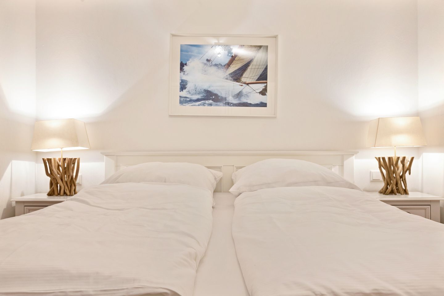 A hotel room with two beds, white bedding, wooden nightstands with lamps, and a framed picture on the wall.