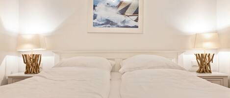 A hotel room with two beds, white bedding, wooden nightstands with lamps, and a framed picture on the wall.