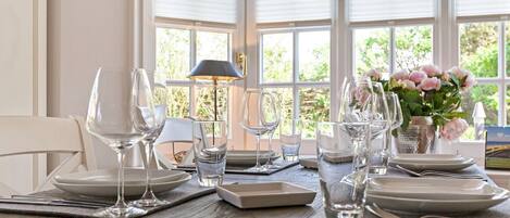 A dining table set with clear glassware and plates, a lamp, and a vase with flowers.