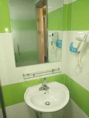 Une salle de bain avec un lavabo blanc, un miroir et un sèche-cheveux fixé au mur.