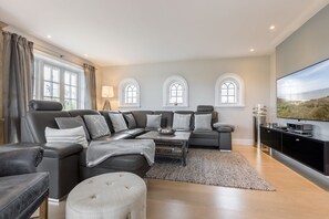 A modern living room with a large sofa, ottoman, and a flat-screen TV.