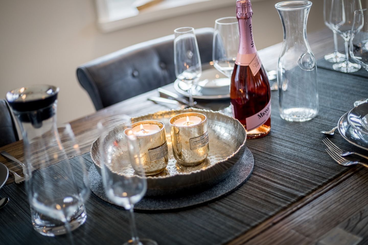 Een eettafel gedekt met kaarsen, een fles wijn en lege glazen.