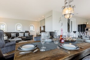 A dining area with a wooden table set for a meal, a chandelier, and a view of the living room with a sofa and arched windows.