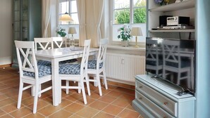 Ein Essbereich mit weißem Tisch und Stühlen, einem Fernseher und einer Schrank mit Regalen.