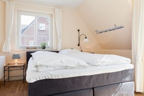 Un dormitorio con cama, una mesita de noche con lámpara, una ventana con cortinas y una pared con placa de identificación.
