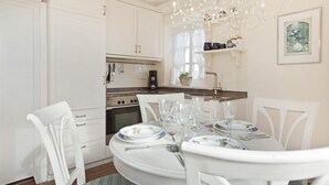 A modern kitchen with white cabinetry, a dining table set for four, and a chandelier. - Friesenhörn, App. 4 Links - Dorfteich. Dünen. Viel Erholung (Wenningstedt-Braderup (Sylt))